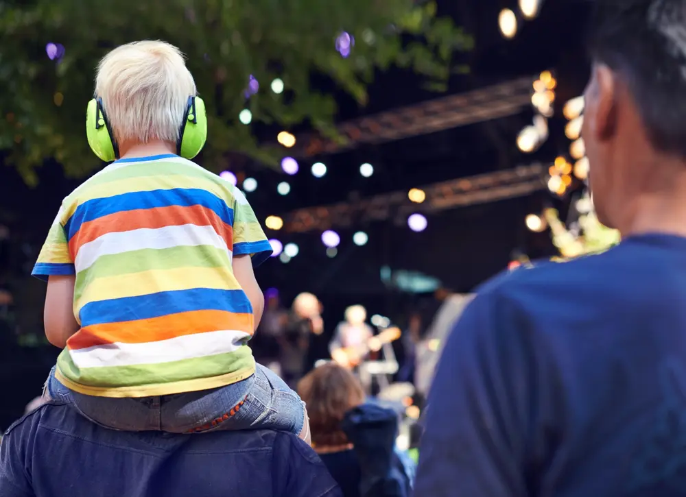 A little boy with green headphones sitting on his father 's shoulders.