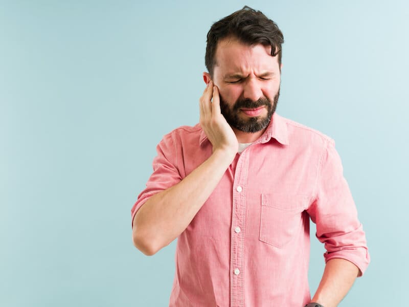 A man in pink shirt holding his ear.