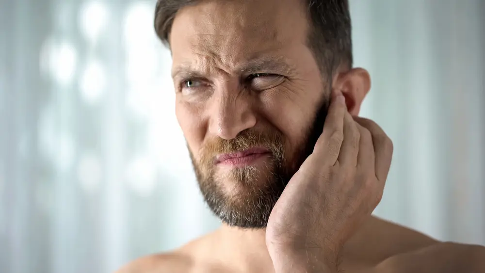 A man with beard and mustache holding his ear.