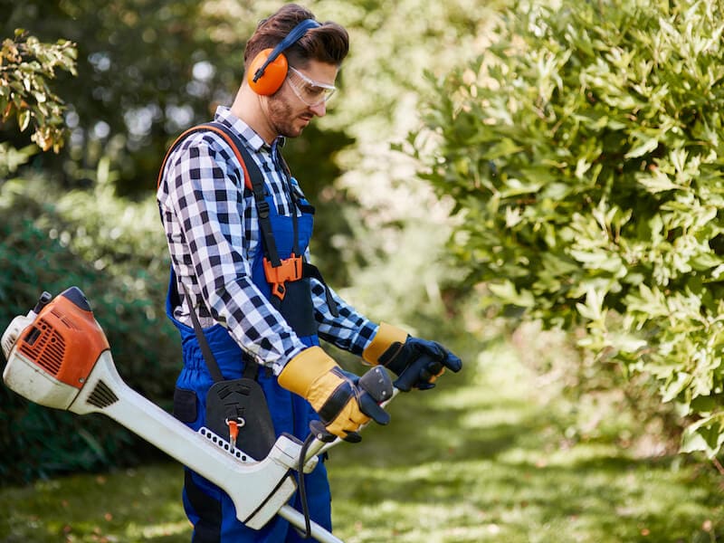 A man holding an electric saw and wearing ear muffs.