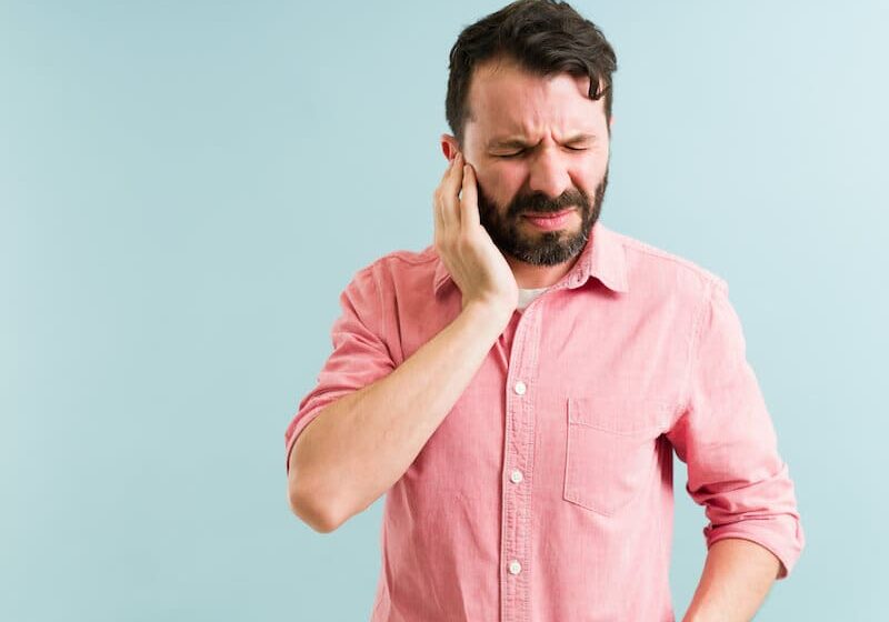 A man in pink shirt holding his ear.