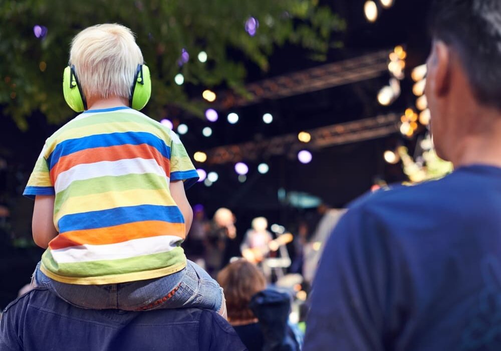 A little boy with green headphones sitting on his father 's shoulders.