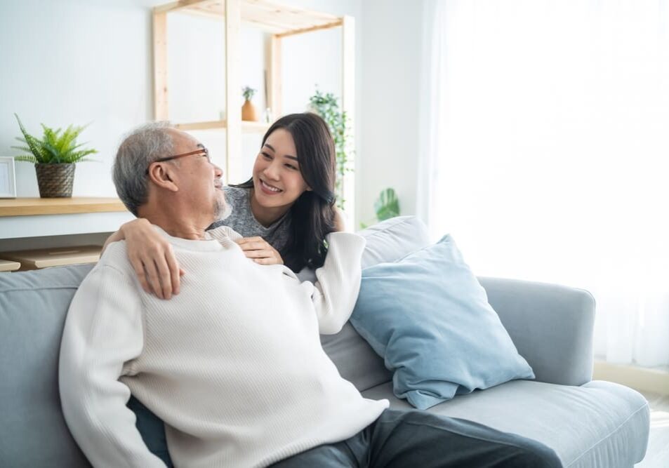 A woman sitting on the arm of an older man.