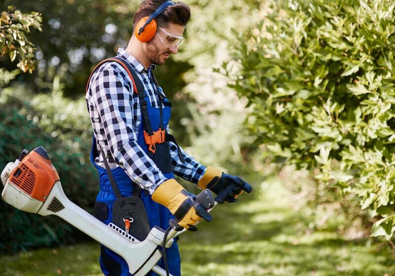 A man holding an electric saw and wearing ear muffs.